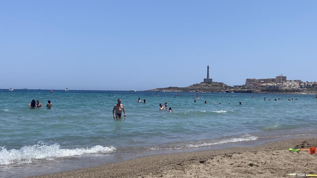 Bañistas en la playa; al fondo, el Faro de Cabo de Palos.