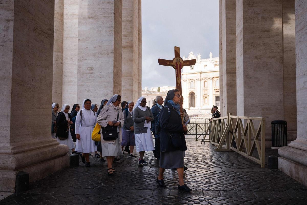 Faithful walk with a cross under the colonnade, a day prior to the start of the conclave,  at the Vatican on May 6, 2025. (Photo by Dimitar DILKOFF / AFP)