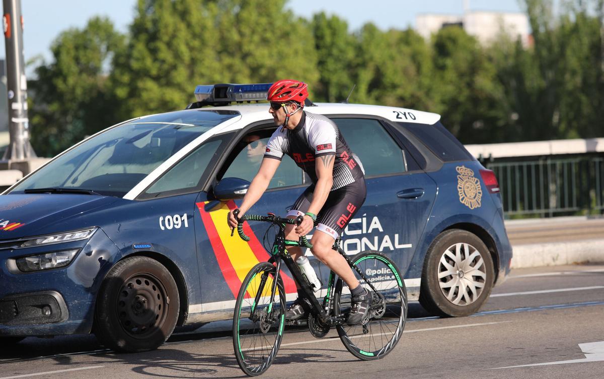 Un ciclista montando en bici a la par que un coche de la Policía Nacional en Zaragoza