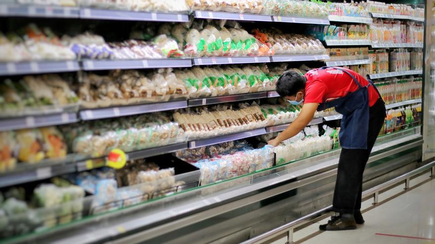 Un empleado de un supermercado repone un frigorífico.