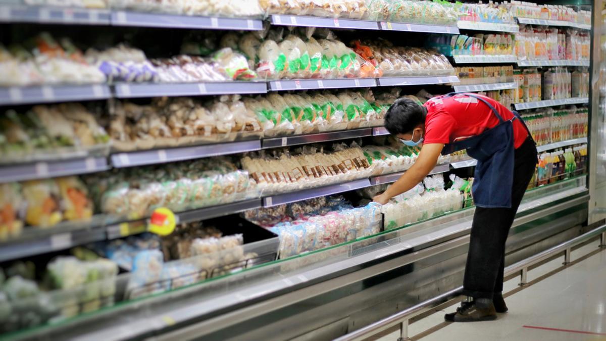 Un empleado de un supermercado repone un frigorífico.