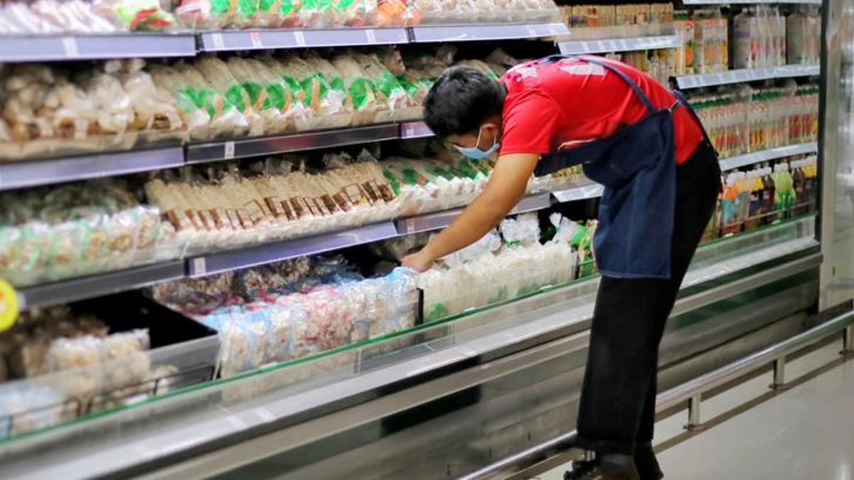 Un empleado de un supermercado repone un frigorífico.