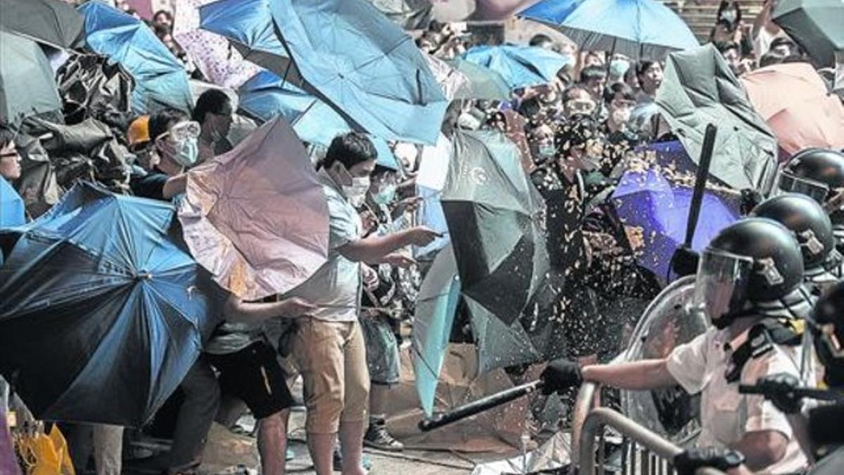 Los agentes lanzan gas pimienta contra los manifestantes, que se protegen con paraguas, el viernes.