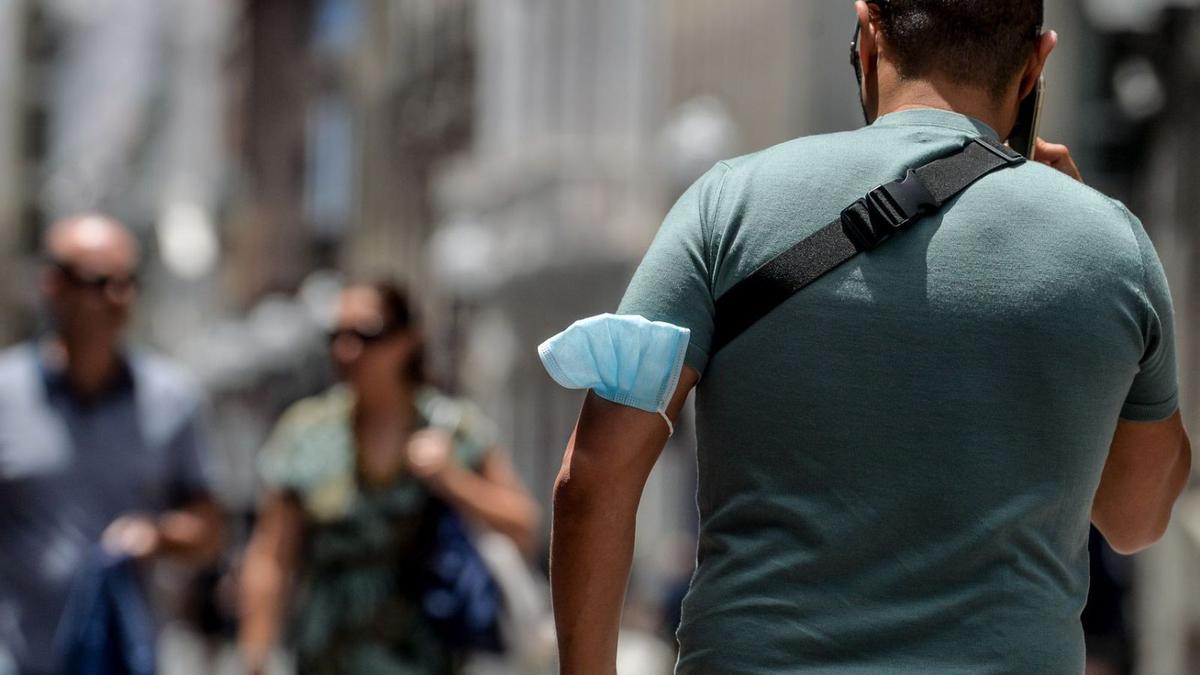 Un joven pasea por una calle capitalina con la mascarilla en el brazo.  | JOSÉ CARLOS GUERRA