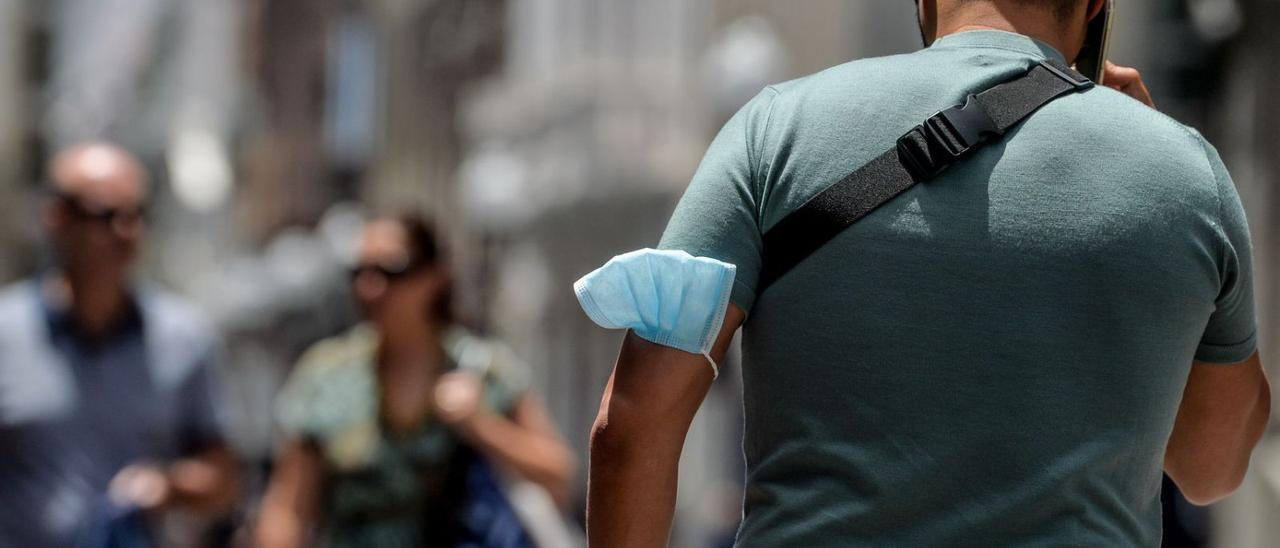 Un joven pasea por una calle capitalina con la mascarilla en el brazo.  | JOSÉ CARLOS GUERRA