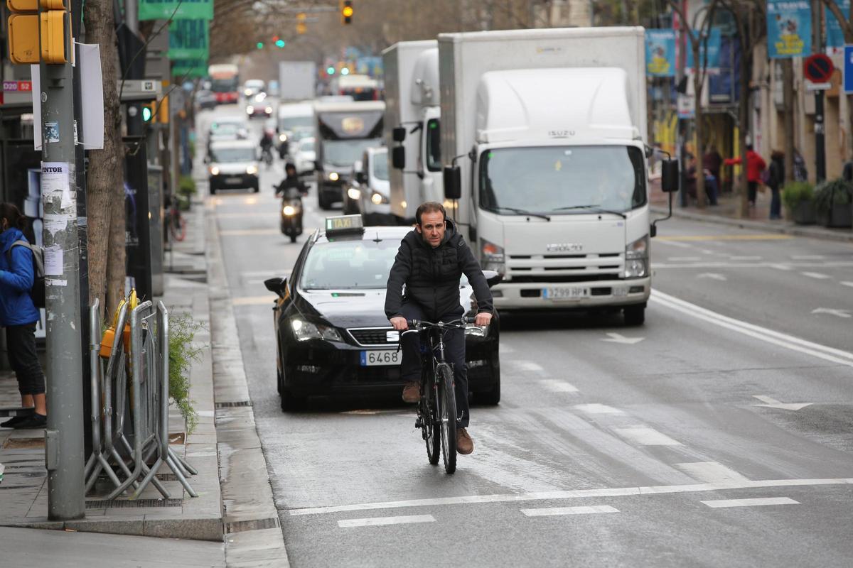 Una bici circula, legalmente, por el carril bus de Creu Coberta. Al fondo, una moto que sí tiene prohibido usar este carril