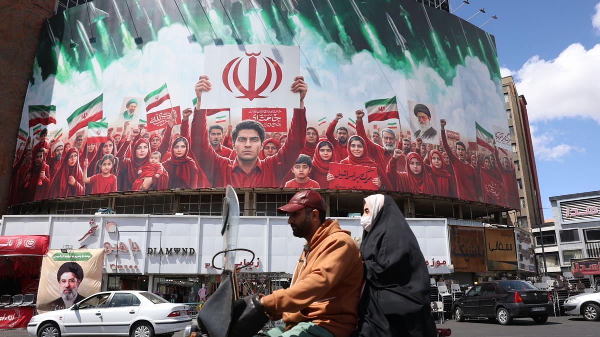 Los transeúntes pasan junto a una valla publicitaria política con los colores de la bandera nacional de Irán en la plaza Valiasr de Teherán, Irán, el 8 de abril de 2026.