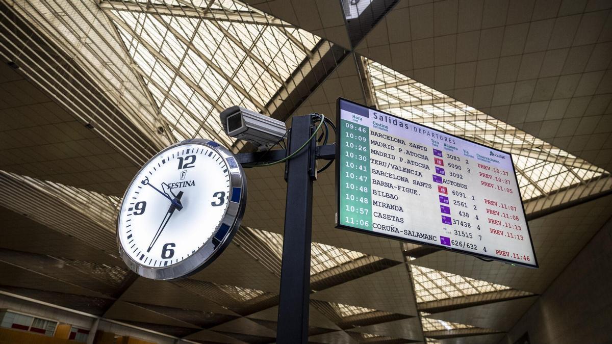 Un reloj y una pantalla de Delicias indicando multitud de retrasos en los trenes en una imagen de archivo