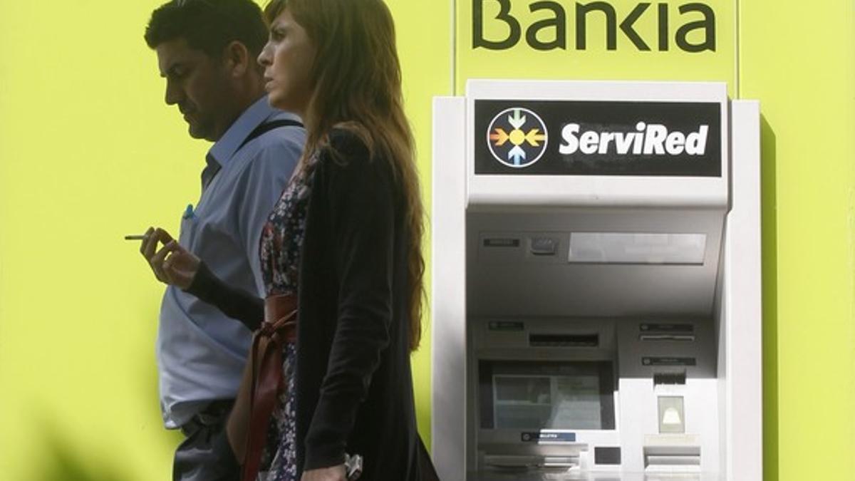 Un hombre y una mujer caminan por un cajero de Bankia