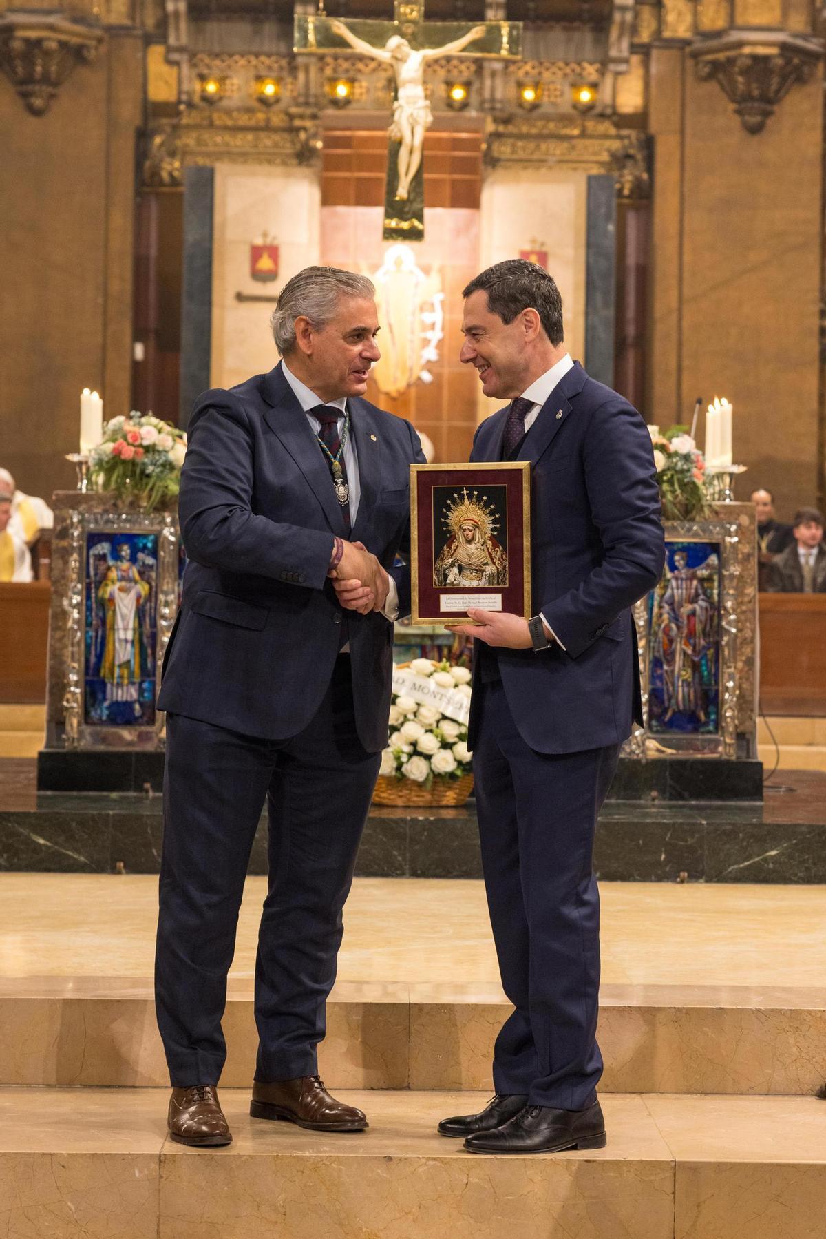 El Hermano Mayor de la Hermandad de Montserrat de Sevilla, Juan Coto, entrega un recuerdo al presidente de la Junta de Andalucía, Juan Manuel Moreno Bonilla