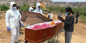 This picture taken on May 8, 2021 shows employees of Michael Undertakers and Ambulance Services (L), seen wearing personal protective equipment (PPE) suits, looking on as a relative stands by a coffin during the burial of a Covid-19 coronavirus victim at a Christian cemetery in Pali village near Faridabad. - As India grapples with a mounting coronavirus death toll, new services ranging from specialist funeral firms, Bollywood film set cleaners and low-budget deliverymen are easing the pain and making a living. (Photo by Sajjad HUSSAIN / AFP) / TO GO WITH INDIA-HEALTH-VIRUS-ECONOMY-STARTUPS,FOCUS BY NIVRITA GANGULY