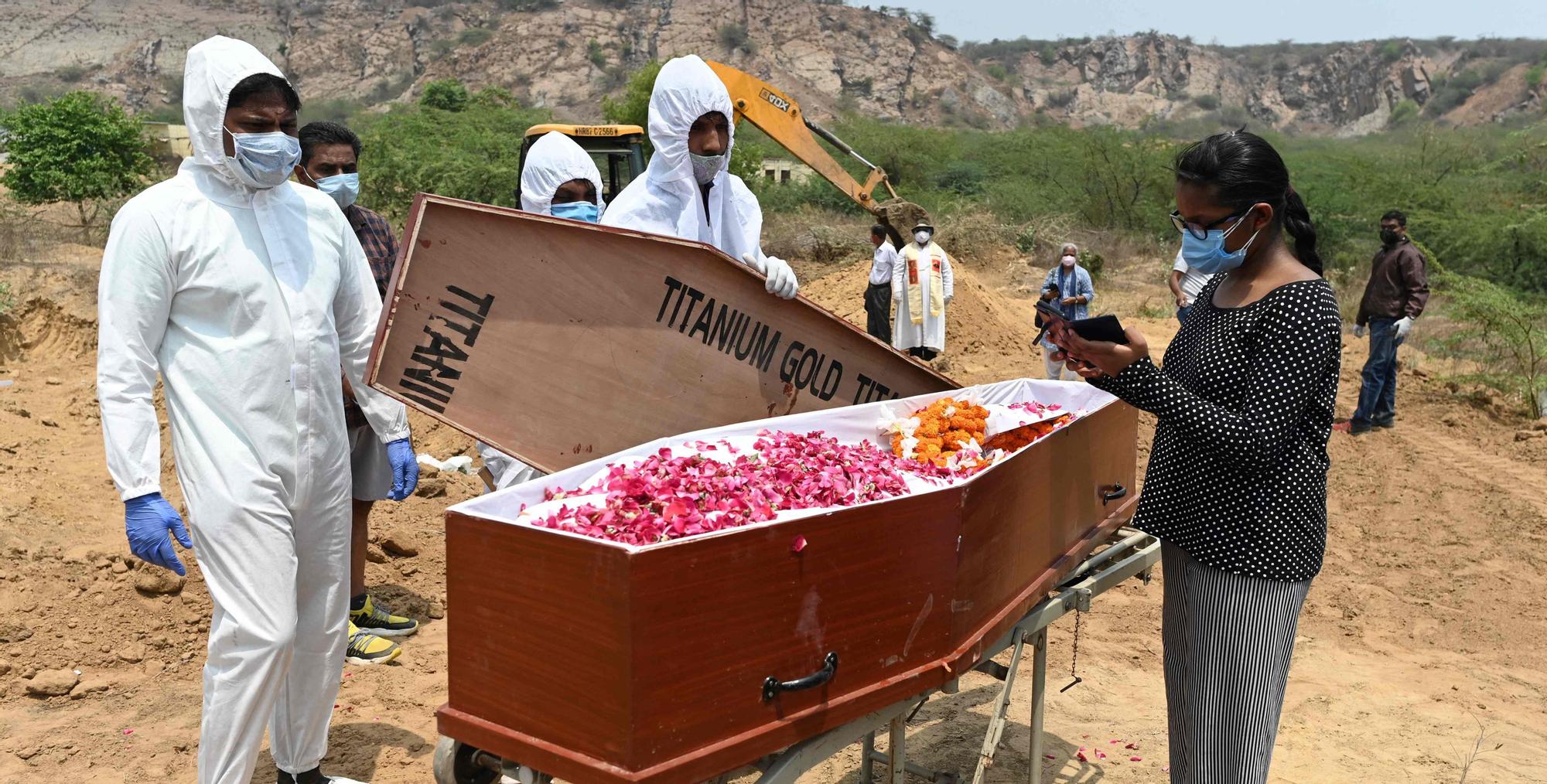 This picture taken on May 8, 2021 shows employees of Michael Undertakers and Ambulance Services (L), seen wearing personal protective equipment (PPE) suits, looking on as a relative stands by a coffin during the burial of a Covid-19 coronavirus victim at a Christian cemetery in Pali village near Faridabad. - As India grapples with a mounting coronavirus death toll, new services ranging from specialist funeral firms, Bollywood film set cleaners and low-budget deliverymen are easing the pain and making a living. (Photo by Sajjad HUSSAIN / AFP) / TO GO WITH INDIA-HEALTH-VIRUS-ECONOMY-STARTUPS,FOCUS BY NIVRITA GANGULY