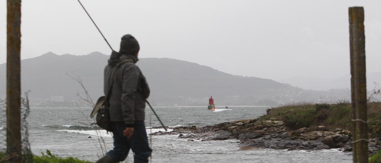 Un pescador observa cómo práctican kite surf, pese al oleaje, junto al faro A Borneira, en Cangas.