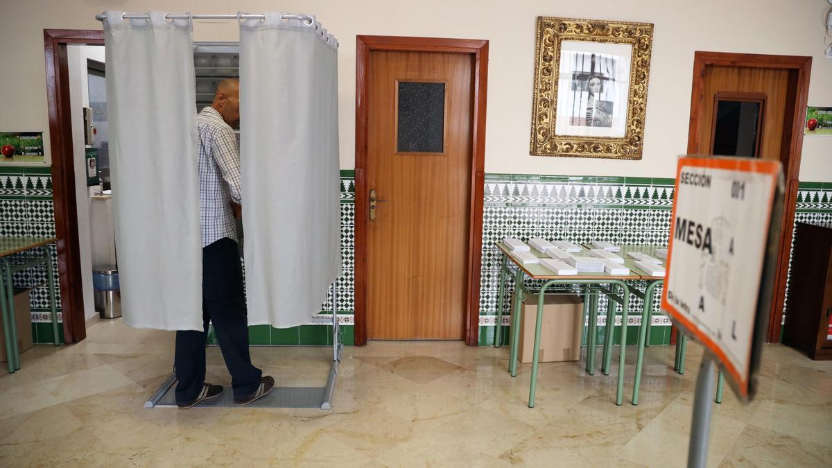 Una persona dentro de una cabina electoral para coger su papeleta para votar, a 28 de mayo de 2023, en Málaga