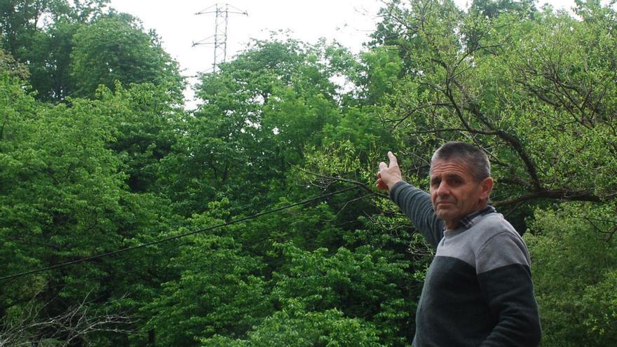 El alcalde de Amieva, Carlos Salazar, señala una de las torres de la línea de alta tensión que avanza por encima de la Casa Consistorial, en la localidad de Precendi.