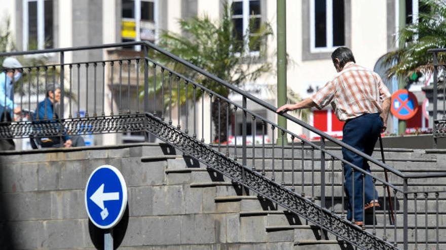 Un señor de edad avanzada sube unas escaleras en la capital grancanaria y un hombre lleva en silla de ruedas a una persona dependiente