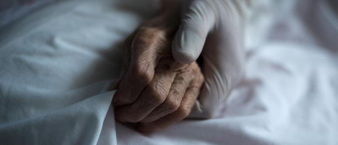 Una cuidadora coge de la mano a una anciana.