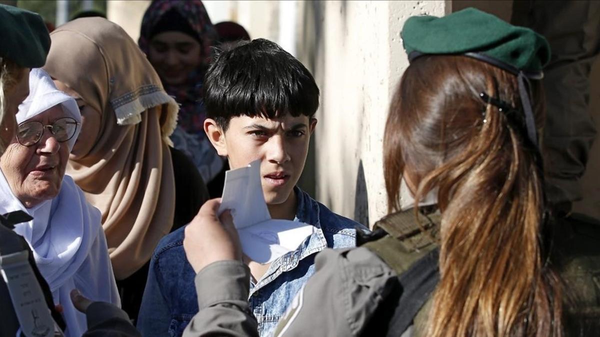 Un nino palestino muestra su carnet de identidad a una agente israeli mientras espera para poder cruzar a Jerusalen a traves del puesto de control de Belen.