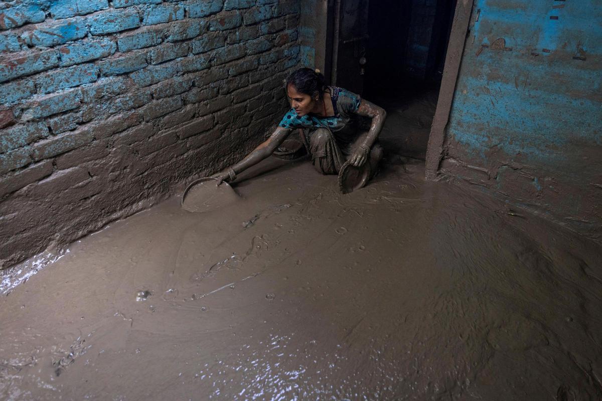 Munni Devi, de 28 años, limpia el barro de la entrada de su casa mientras el agua de la inundación retrocede en una zona residencial que quedó inundada por el desbordamiento del río Yamuna tras las fuertes lluvias, en Nueva Delhi, India, el 17 de julio de 2023.