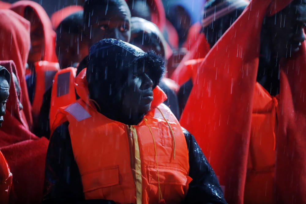 Migrants stand under the rain on a rescue boat ...