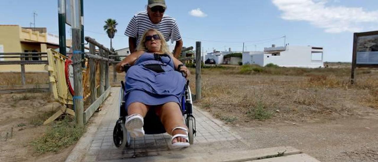 Un hombre empuja la silla de una usuaria para subir el escalón y acceder así al punto accesible de la playa de Almardà.