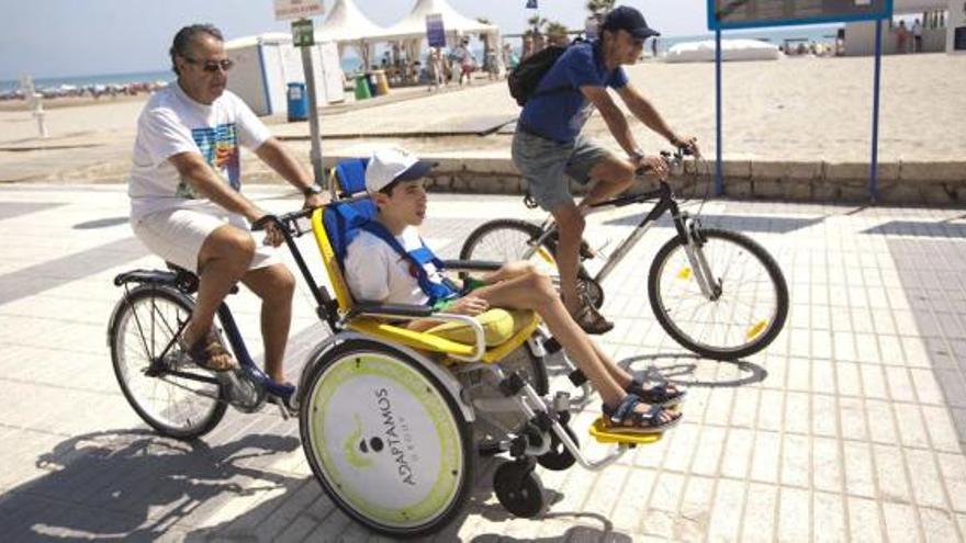 El abuelo de un discapacitado pasea a su nieto en la playa de San Juan gracias a un prototipo de bicicleta adaptada.