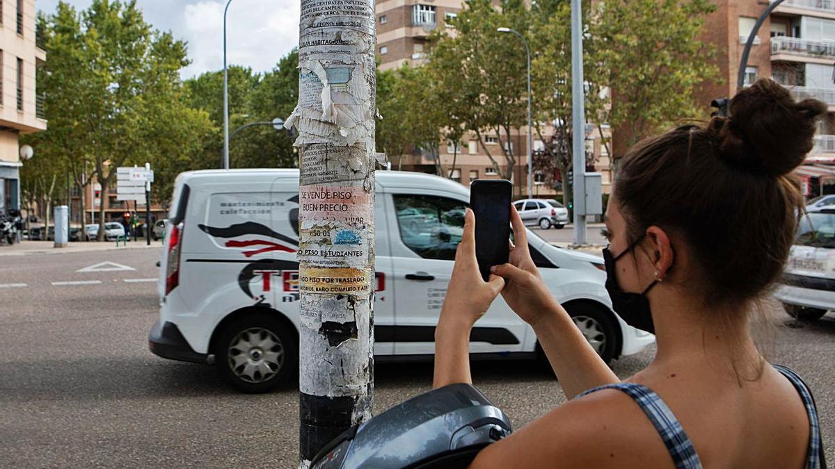 Una joven fotografía diferentes anuncios para compartir piso pegados en una farola.