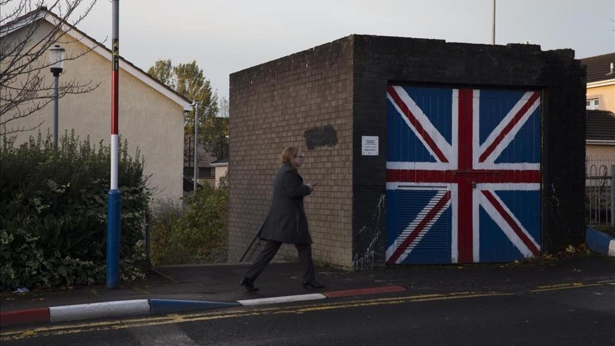 Una mujer pasa junto a un muro que luce la bandera de la Union Jack, en el barrio de Fountain West, en la localidad norirlandesa de Derry.