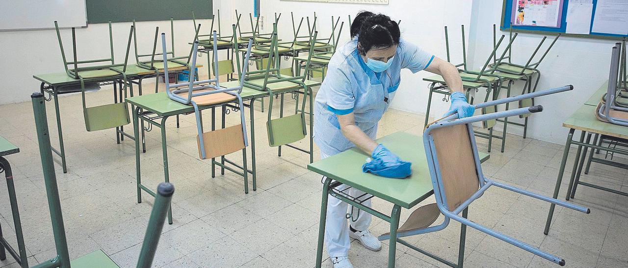 Una trabajadora limpia un aula de un colegio.