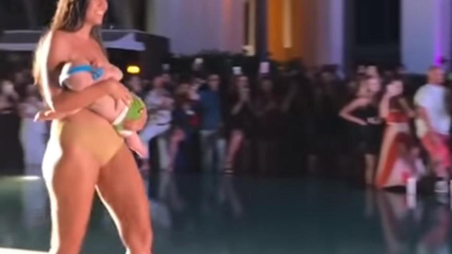 Una modelo da el pecho a su bebé durante un desfile de bañadores