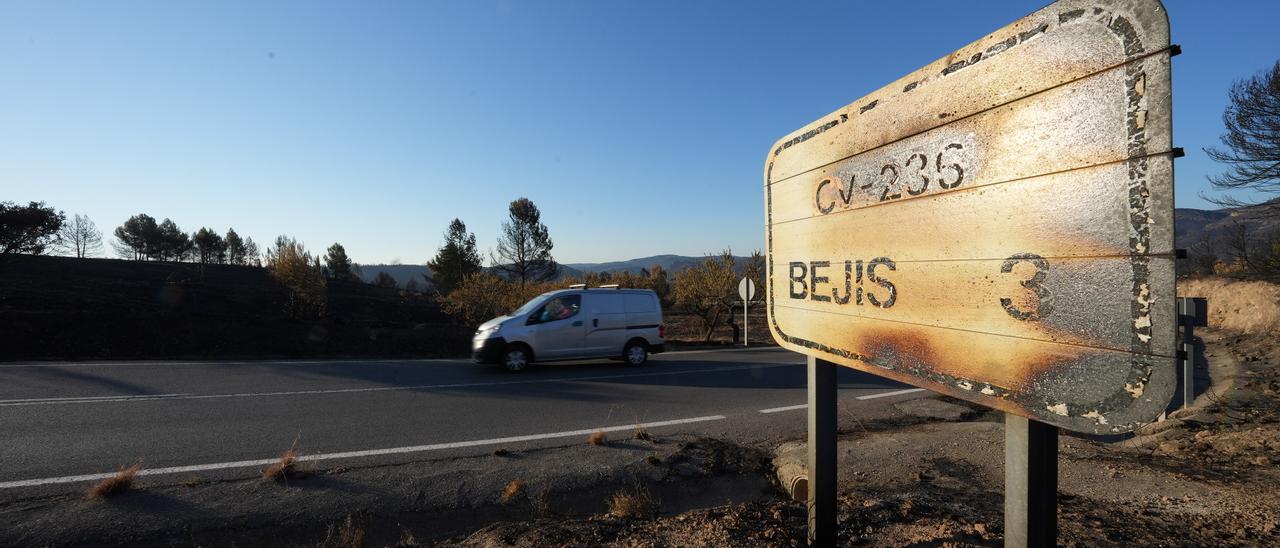 Un automóvil pasa por una carretera con árboles y señalas afectadas por el fuego.