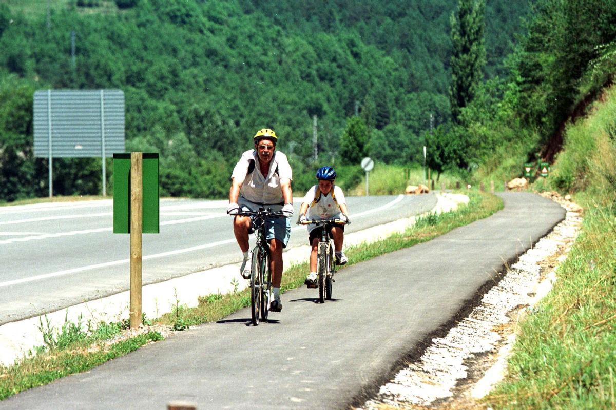 Dos ciclistas circulan por un carril bici junto a una carretera, en Girona.