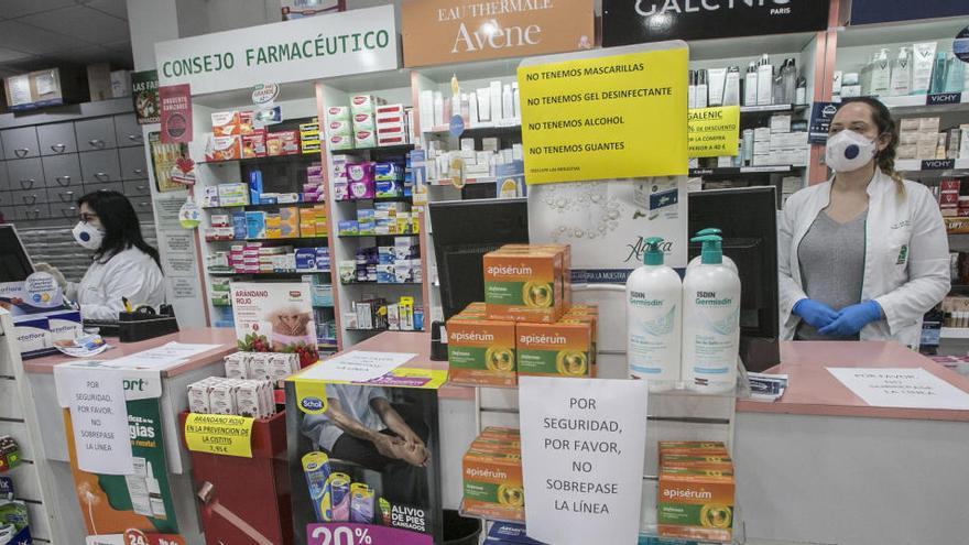 Profesionales atienden con mascarilla en una farmacia de Alicante y se lee un cartel en el que avisan de que no tienen mascarillas