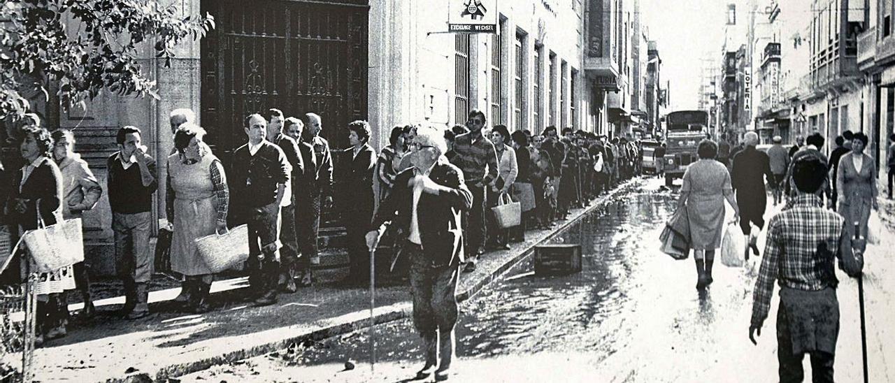 Cola de damnificados en busca de víveres en la calle Pérez Galdos de Alzira. | «AIGUA, FANG, POR I DOLOR»