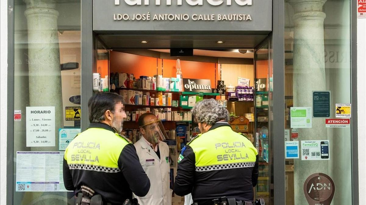 Dos agentes de la polícia local de Sevilla hablan con un farmacéutico en la puerta de su local