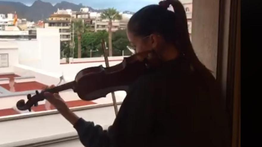 La violinista Ana Alonso Gutiérrez toca el violín desde una ventana de su casa.