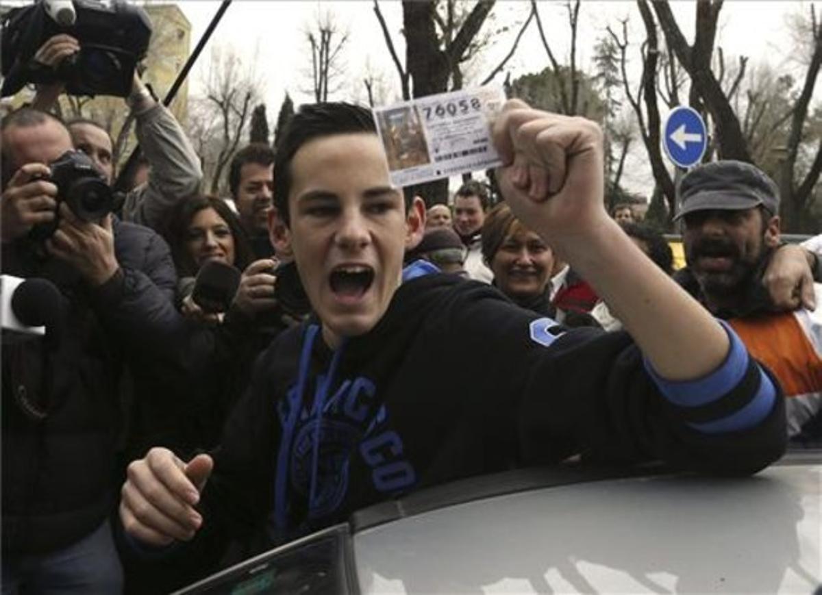 Un noi mostra un dècim del número 76.058 que ha estat afavorit amb el primer premi de la Loteria de Nadal comprat a Alcalá.