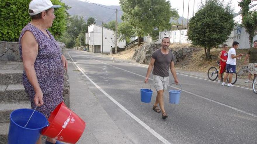 Dos vecinos portan cubos para abastecerse de agua.