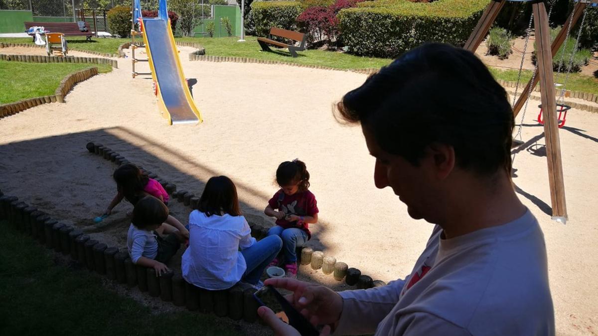 Javier mira su móvil mientras sus hijas juegan con dos amigos en un parque cercano a su casa, en Madrid.
