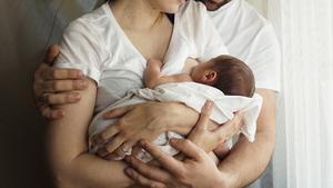 Una madre amamanta a su bebé en casa, junto a su pareja.