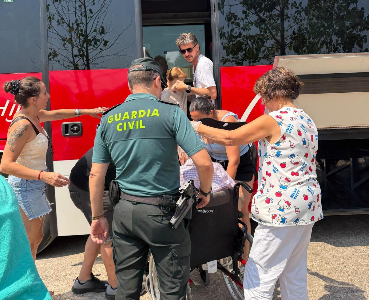 Un agente de la Guardia Civil ayuda a unos vecinos a bajar del autobús en el que fueron trasladados a su pueblo.