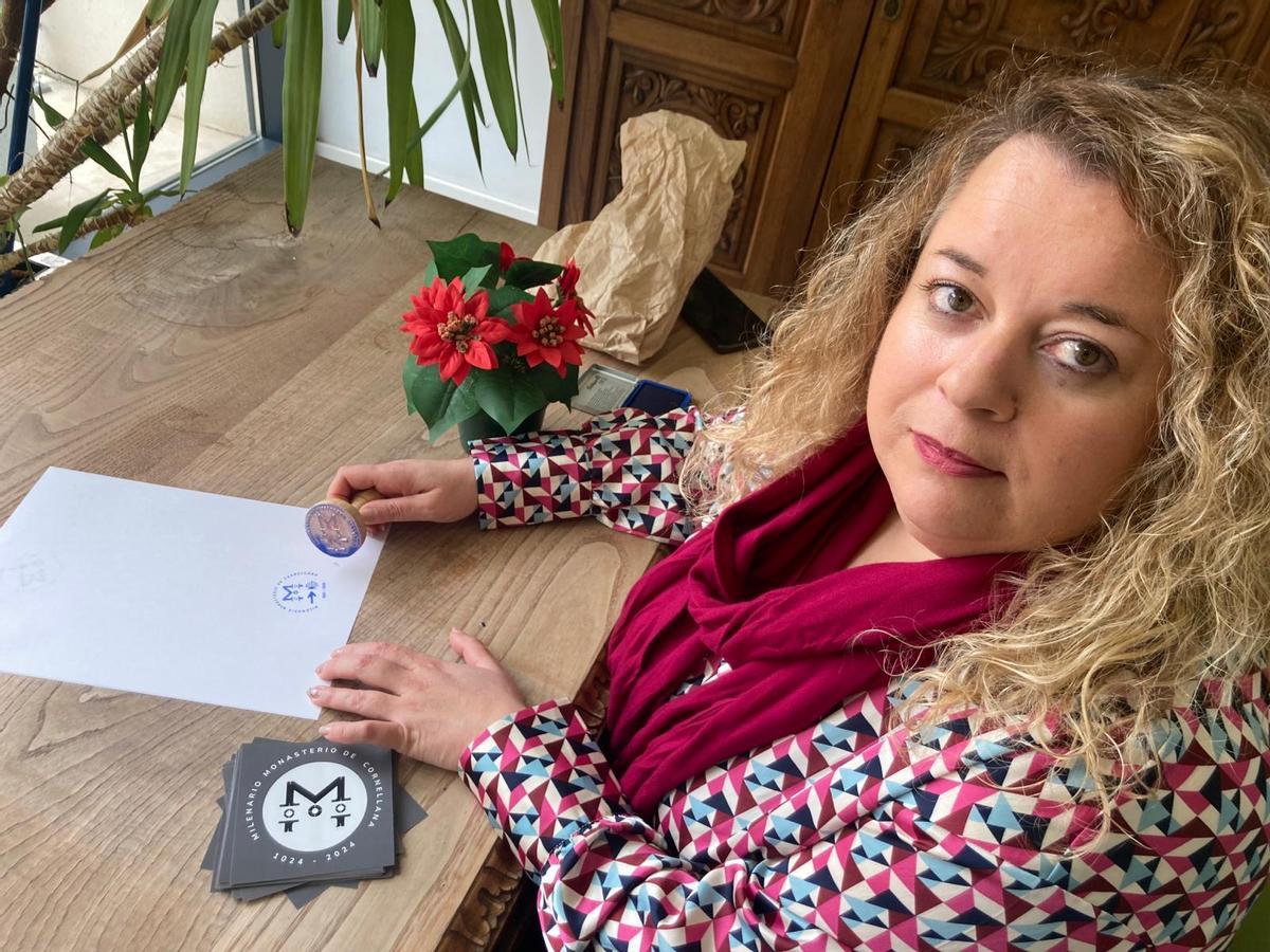 La concejala Ana Pérez muestra el sello especial del milenario y las pegatinas conmemorativas que se repatirán entre los negocios de la zona
