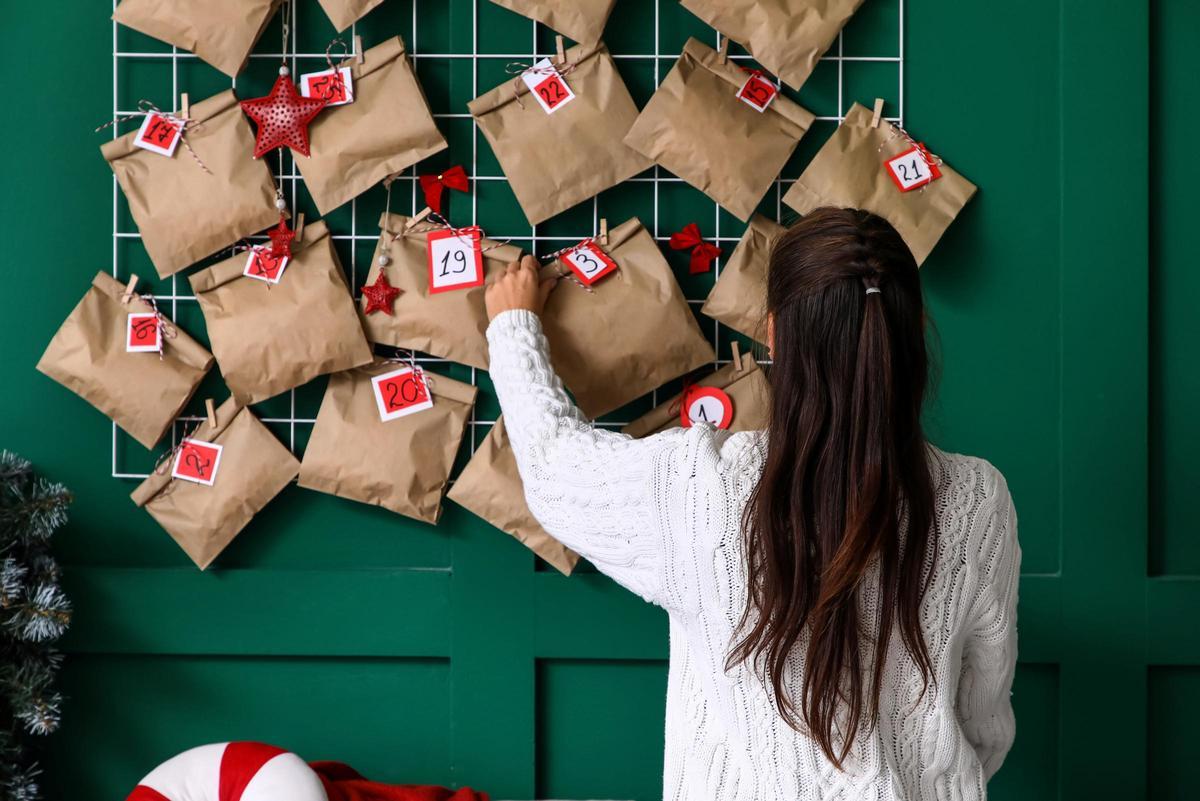 Mujer con el calendario de Adviento de Navidad en la pared verde en casa, vista trasera
