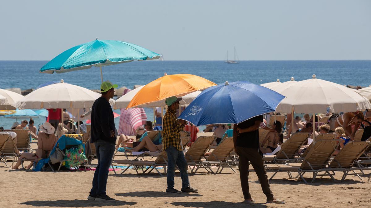 Varias personas se protegen del sol en la playa de la Barceloneta
