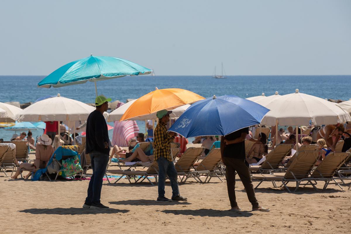 Varias personas se protegen del sol en la playa de la Barceloneta