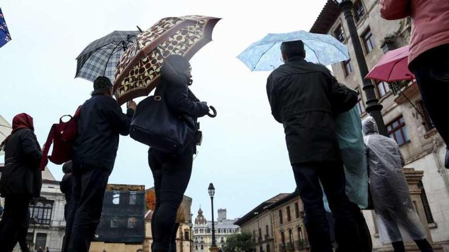 Un grupo de visitantes, ayer por la tarde, bajo la lluvia, en la plaza de la Catedral, en Oviedo.