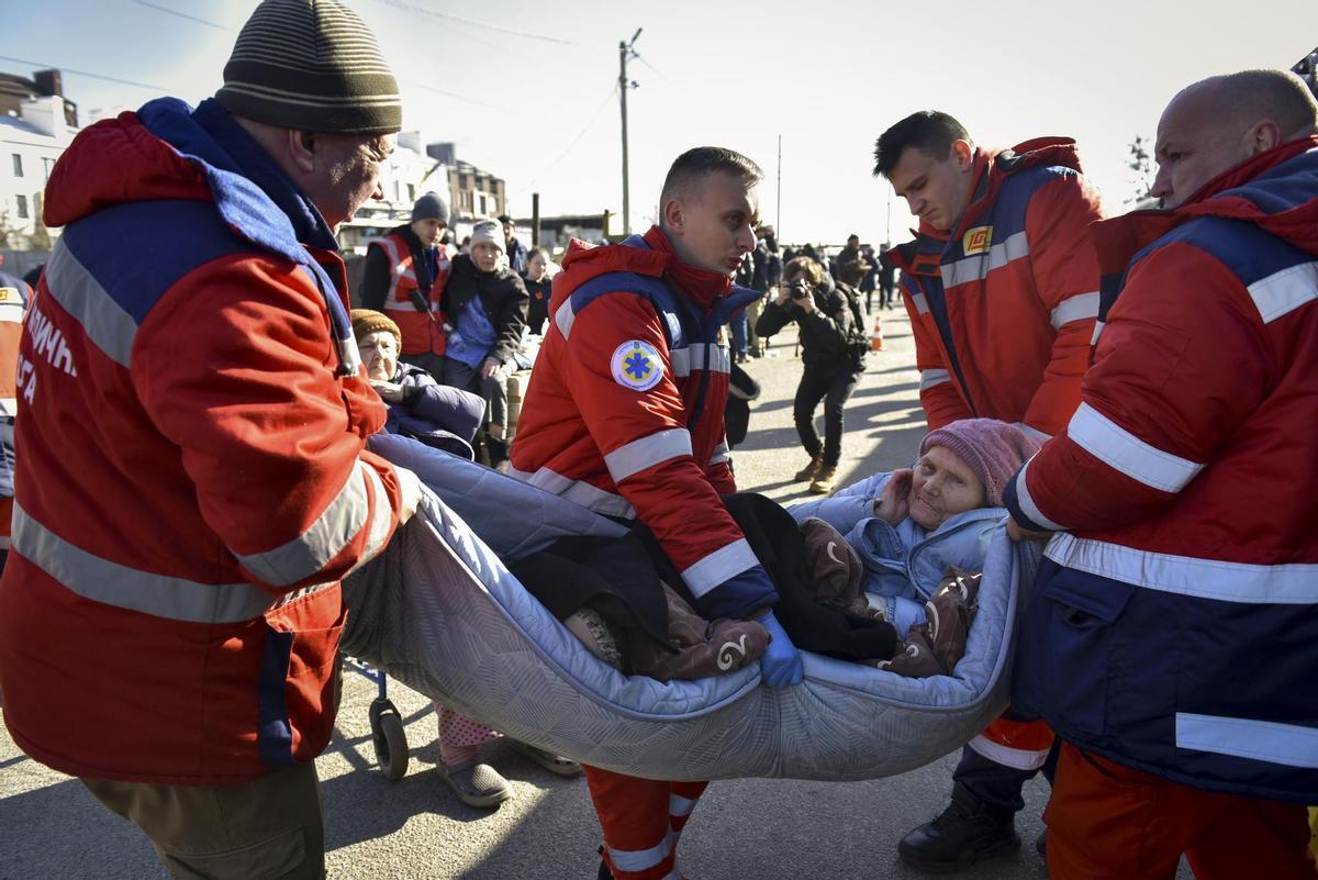 Varias personas del servicio de emergencias en Ucrania ayudan a una anciana.