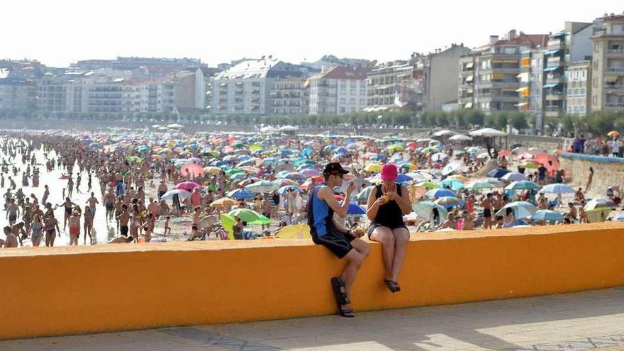 Dos turistas toman un helado sentados en el muro de la playa de Silgar, abarrotada de bañistas. // Gustavo Santos