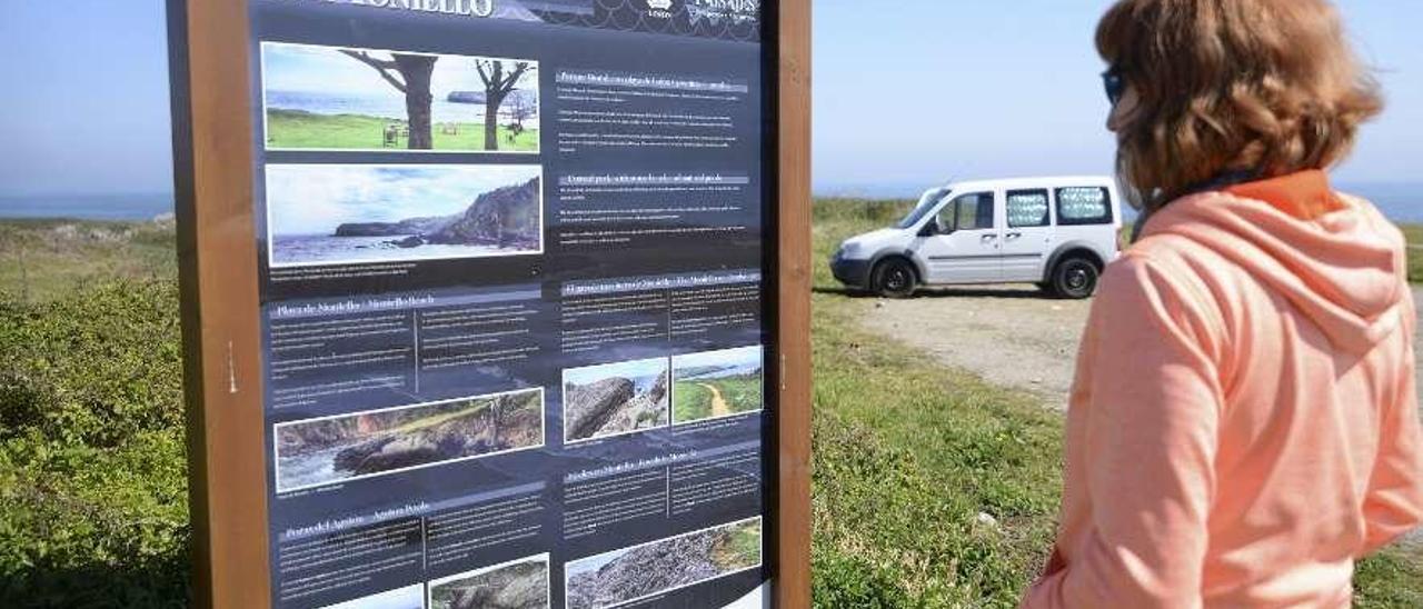 Una mujer lee el panel turístico ubicado junto a la playa de Moniello.