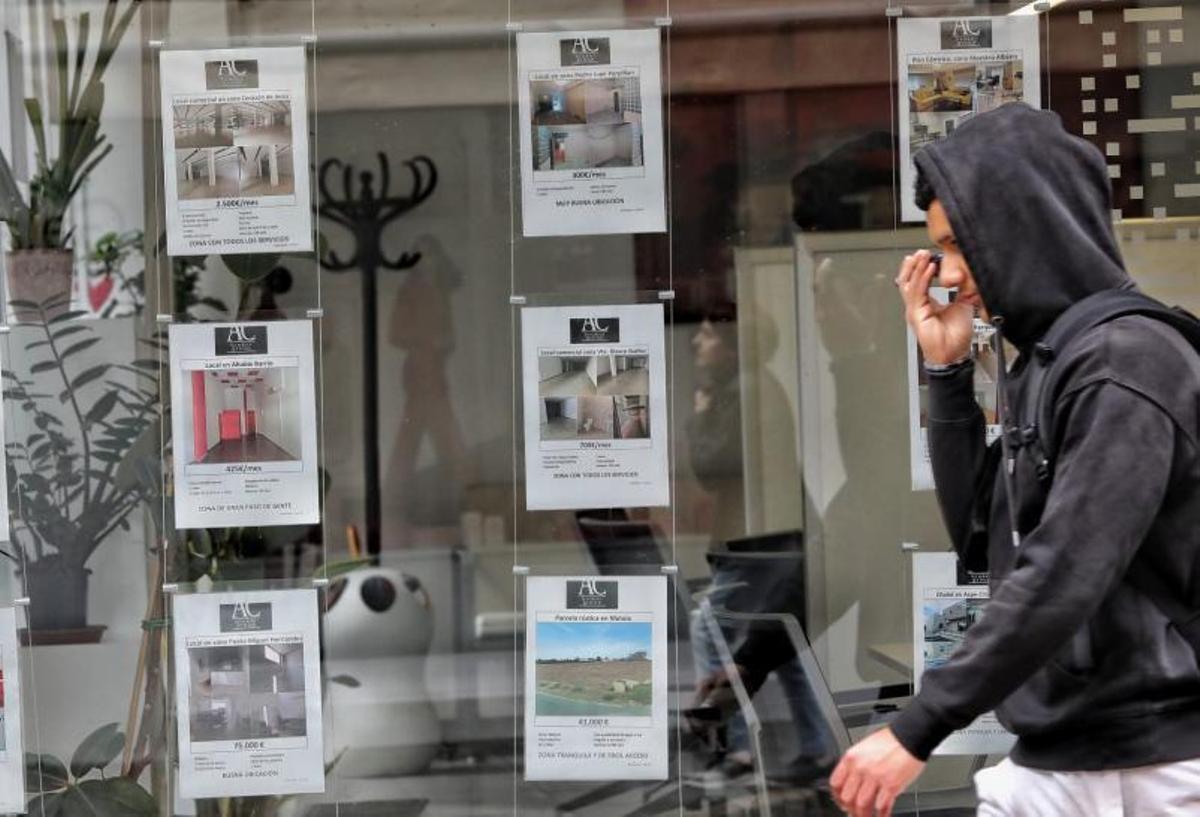 Un joven pasa por delante de una inmobiliaria de Elche donde se anuncian pisos en alquiler y a la venta. | ANTONIO AMORÓS
